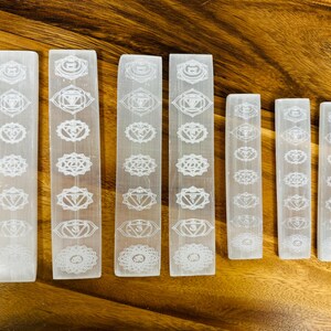 May include: Seven white selenite wands with etched chakra symbols. The wands are arranged in order from largest to smallest.