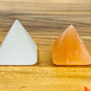 May include: Two small crystal pyramids, one white and one orange, on a wooden surface.