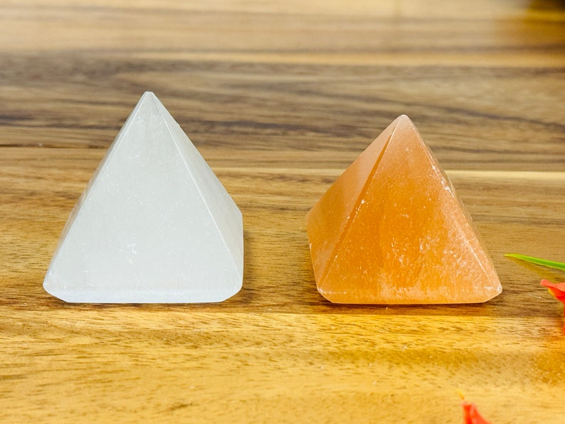 May include: Two small crystal pyramids, one white and one orange, on a wooden surface.