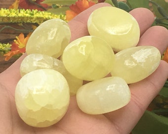 May include: A collection of seven smooth, pale yellow tumbled stones. The stones are oval shaped and have a slightly translucent appearance.