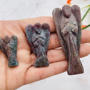May include: Three carved angel figurines in varying sizes. The angels are made of a stone material with a mix of red, gray, and green hues. The angels have their hands clasped in front of them and wings spread out.