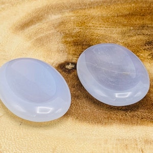May include: Two smooth, oval-shaped blue agate stones. The stones are polished and have a light blue color.