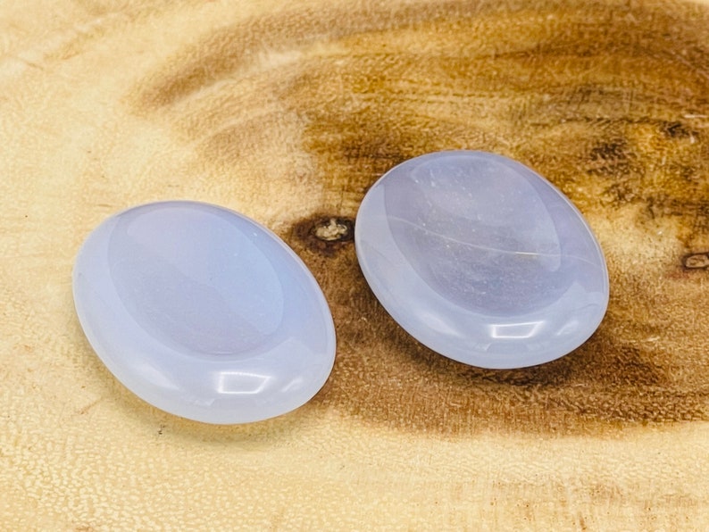 May include: Two smooth, oval-shaped blue agate stones. The stones are polished and have a light blue color.