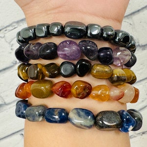 Puede incluir: Una pila de siete pulseras hechas de varias piedras preciosas, incluyendo hematita negra, amatista, ojo de tigre, cornalina y lapislázuli.
