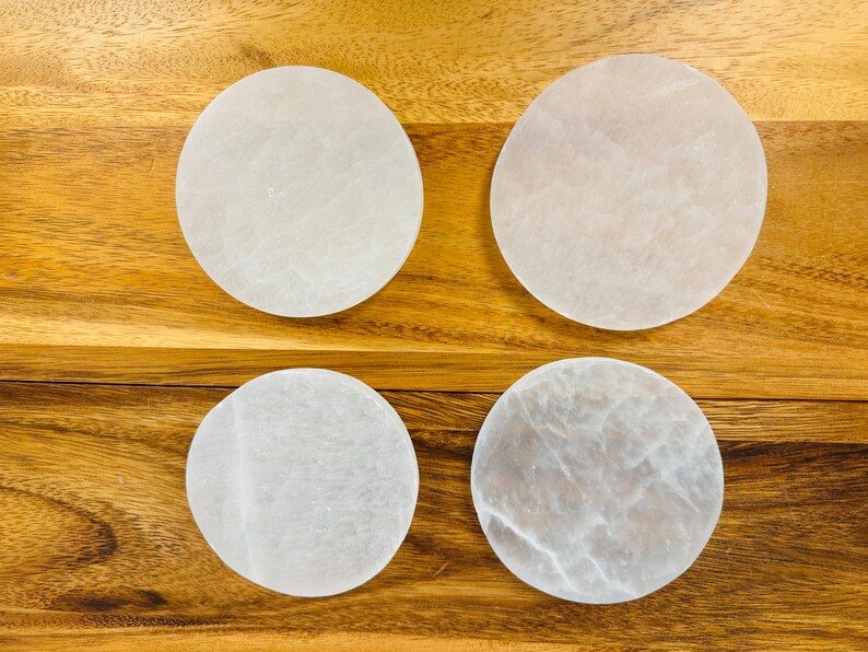 May include: Four white selenite charging plates on a wooden surface. The plates are round and have a smooth, polished finish.