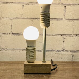 May include: A DIY lamp made from two LED light bulbs and a metal rod. The lamp is mounted on a rectangular stone base and has a black cord.