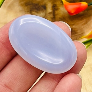May include: A smooth, light blue, oval-shaped, polished gemstone. The stone is held in a hand.