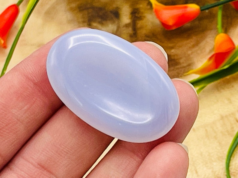 May include: A smooth, light blue, oval-shaped, polished gemstone. The stone is held in a hand.