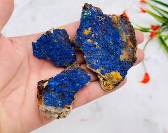 May include: Three raw azurite mineral specimens featuring deep royal blue crystalline surfaces with patches of earthy brown and tan matrix. The stones have a rough, textured appearance with visible clusters of vibrant blue mineral formations.