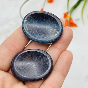 May include: Two blue and black polished gemstone palm stones. The stones are smooth and have a slightly concave shape.