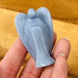 May include: A small, light blue angel figurine carved from a smooth, polished stone. The angel has wings and a simple, rounded head.