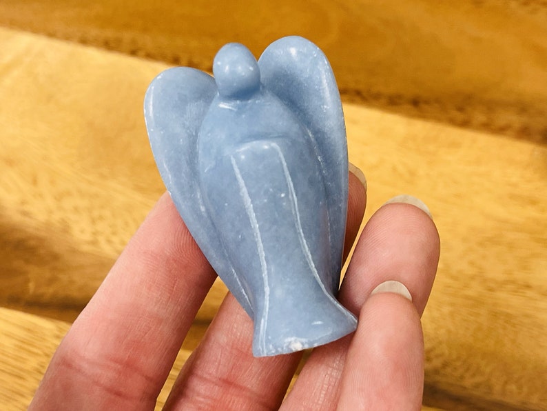 May include: A small, light blue angel figurine carved from a smooth, polished stone. The angel has wings and a simple, rounded head.