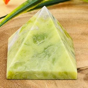 May include: A green and white pyramid-shaped crystal. The crystal has a smooth, polished surface and a swirling pattern.