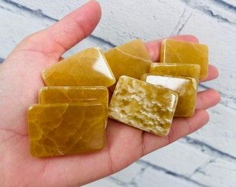 May include: A collection of seven yellow calcite crystal slices, each with a unique pattern and texture. The slices are arranged in a hand, showcasing their natural beauty.