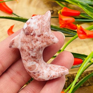 Puede incluir: Una figurita de delf&iacute;n tallada en m&aacute;rmol rosa y blanco. El delf&iacute;n est&aacute; en una pose de salto con la cola enroscada alrededor de su cuerpo.