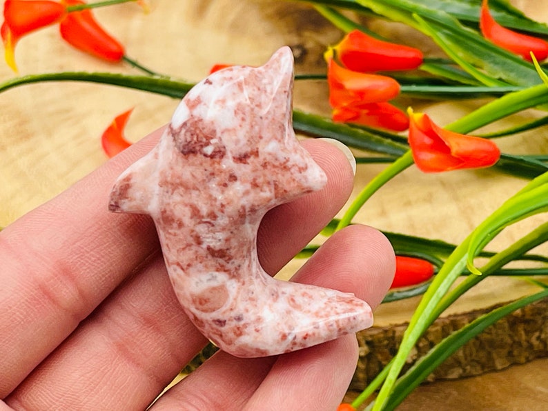 Puede incluir: Una figurita de delf&iacute;n tallada en m&aacute;rmol rosa y blanco. El delf&iacute;n est&aacute; en una pose de salto con la cola enroscada alrededor de su cuerpo.