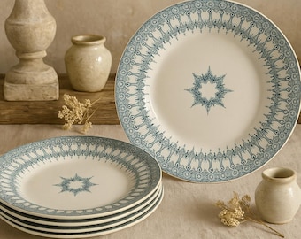 May include: A stack of four white ceramic plates with a blue ornate border and a starburst design in the center. A fifth plate is standing upright. The plates are part of a dinnerware set.