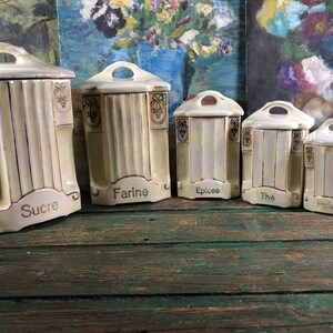 Peut inclure: Ensemble de cinq pots en céramique vintage avec des garnitures dorées et des étiquettes. Les étiquettes indiquent "Sucre", "Farine", "Epices", "Thé" et "Poivre".