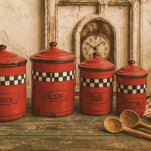 Puede incluir: Cuatro botes de cocina rojos vintage con bandas a cuadros blancos y negros, etiquetados como "Sucre", "Farine", "Cafe" y "Gicorée". Dos cucharas de madera y un paño a cuadros sobre una superficie de madera.