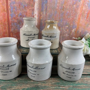 Puede incluir: Cinco botellas antiguas de cerámica, de forma cilíndrica y con bordes anchos. Las botellas blanquecinas presentan texto en tinta negra, incluyendo "Hainault-Monnet, AVALLON" y el año "1750".