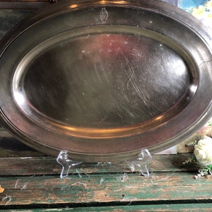 Puede incluir: Un plato de servir ovalado grande de plata con un borde ligeramente elevado. El plato tiene una superficie lisa y brillante con algunos arañazos.