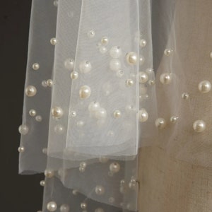 May include: A white tulle veil with pearl embellishments. The veil is layered and has a delicate, romantic look.