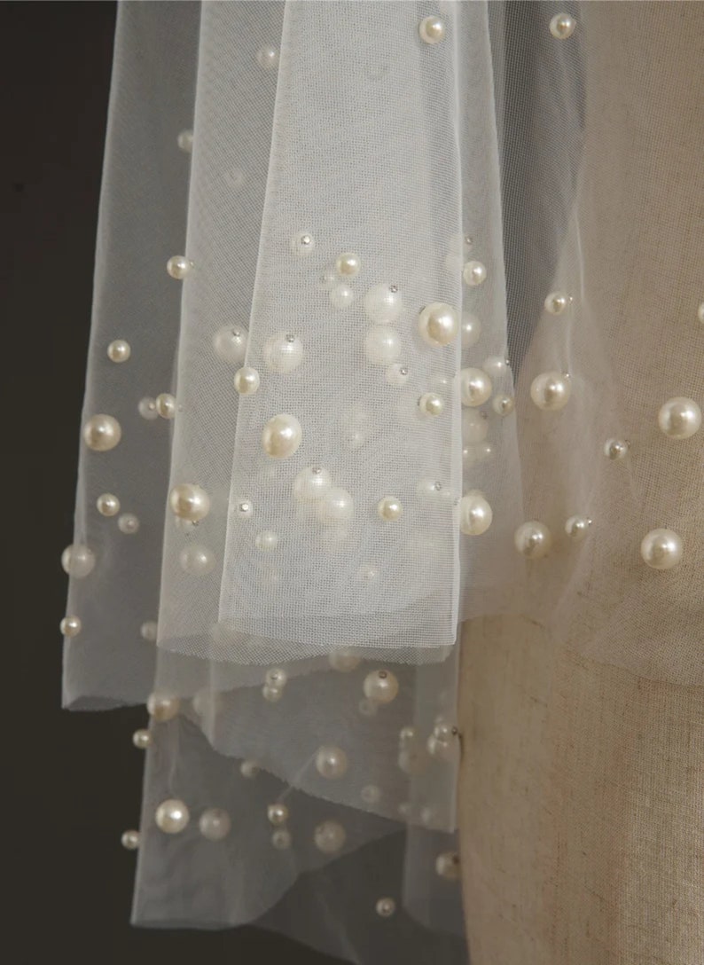 May include: A white tulle veil with pearl embellishments. The veil is layered and has a delicate, romantic look.