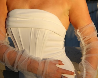 Può includere: Abito da sposa bianco senza spalline con corpetto aderente e gonna fluida. L'abito presenta maniche a sbuffo trasparenti. Il testo "Daisy BridalShop" è visibile. Tema: moda nuziale.
