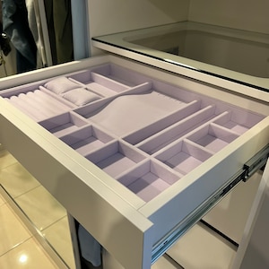 May include: A white drawer with a light purple velvet liner divided into compartments for storing jewelry. The drawer is open and the compartments are visible.