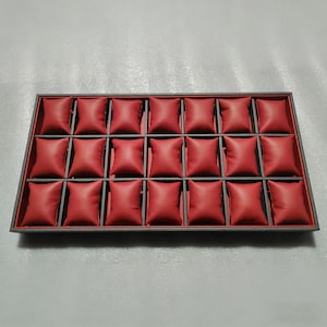 May include: A rectangular watch display case with a grey frame and a red interior. The interior is divided into 20 compartments, each with a red pillow. The case is designed to hold and showcase watches, ideal for retail or personal use.