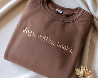 May include: A white ceramic mug with a black handle and the text "But First, Coffee" in a bold, black font. The mug is set against a blurred background, suggesting a cozy setting. The mug appears to be approximately 4 inches tall.