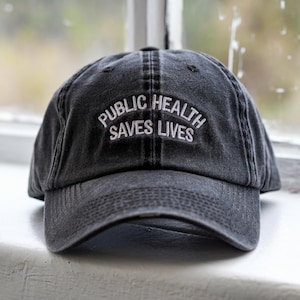 May include: A black denim baseball cap with white embroidery that reads "Public Health Saves Lives".