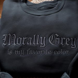 Peut inclure: Sweat-shirt gris fonc&eacute; avec la phrase brod&eacute;e "Morally Grey is my favorite color" en police gothique. Le sweat-shirt est de couleur unie et semble &ecirc;tre fait d'une mati&egrave;re douce.