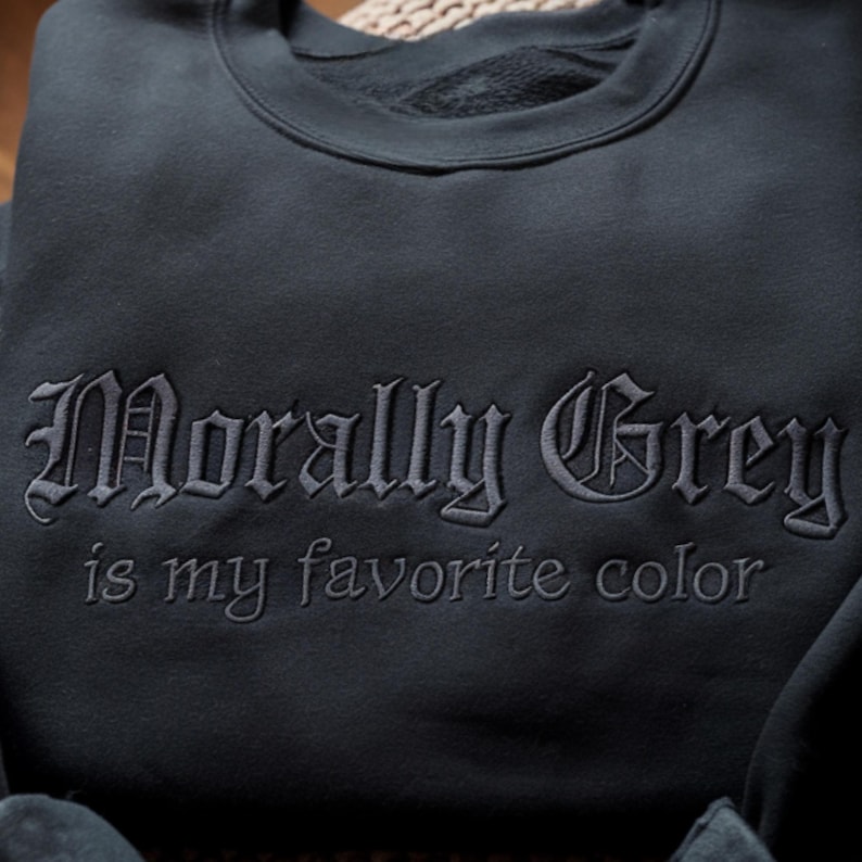 Peut inclure: Sweat-shirt gris fonc&eacute; avec la phrase brod&eacute;e "Morally Grey is my favorite color" en police gothique. Le sweat-shirt est de couleur unie et semble &ecirc;tre fait d'une mati&egrave;re douce.