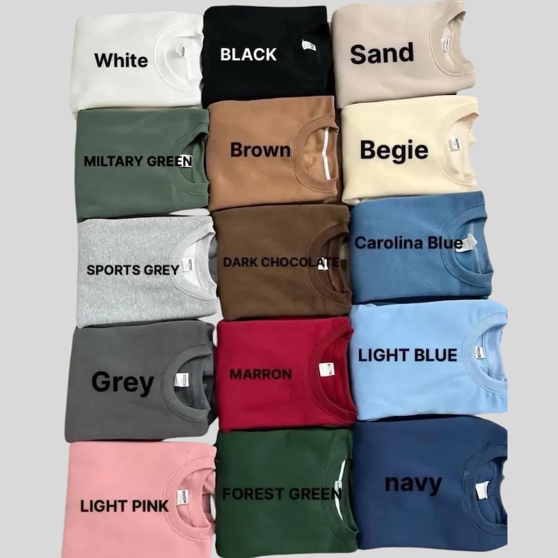 May include: A collection of folded crewneck sweatshirts in various colors, including white, black, sand, military green, brown, beige, sports grey, dark chocolate, grey, maroon, forest green, navy, light pink, carolina blue, and light blue. Each sweatshirt has a tag with its color name.