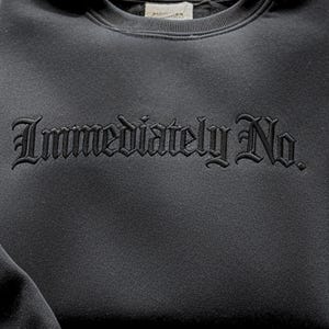 May include: A dark gray sweatshirt with the embroidered text "Immediately No" in a gothic font. The sweatshirt has a crew neck and a soft, textured appearance. The design is centered on the chest.