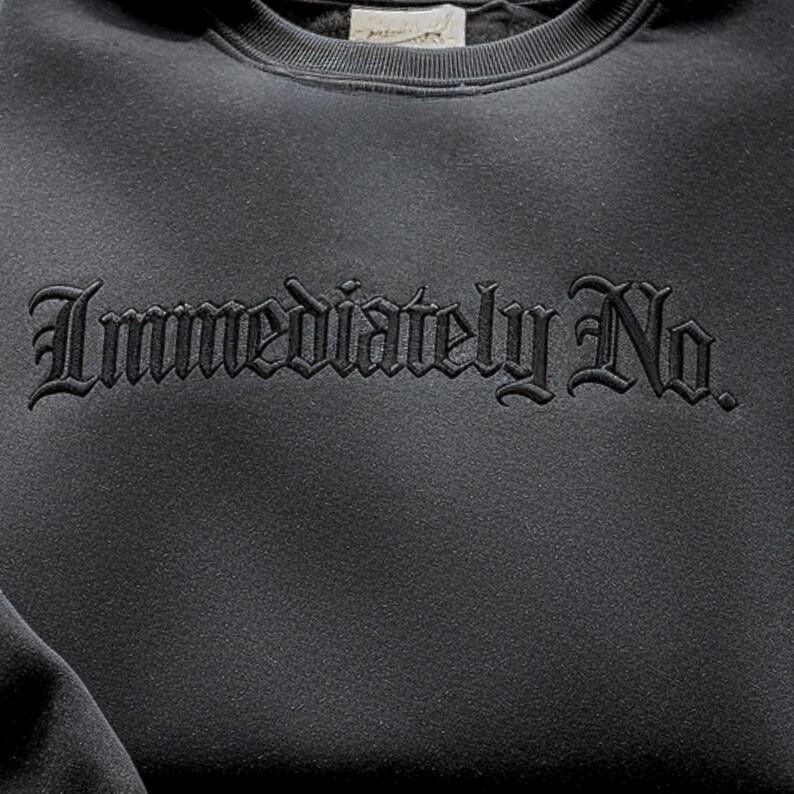 May include: A dark gray sweatshirt with the embroidered text "Immediately No" in a gothic font. The sweatshirt has a crew neck and a soft, textured appearance. The design is centered on the chest.