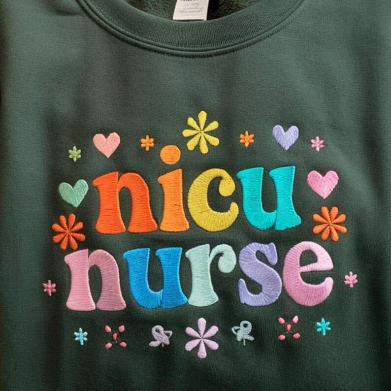 Puede incluir: Sudadera verde oscuro con texto bordado y detalles florales. El texto dice "NICU Nurse" en colores del arco&iacute;ris. El dise&ntilde;o incluye corazones y flores en varios colores, creando un tema alegre y de apoyo.