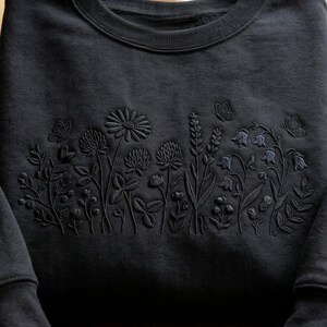 May include: Black sweatshirt with embroidered floral design. The design features various flowers, leaves, and butterflies in a tone-on-tone color scheme. The crew neck sweatshirt is made of a soft material.