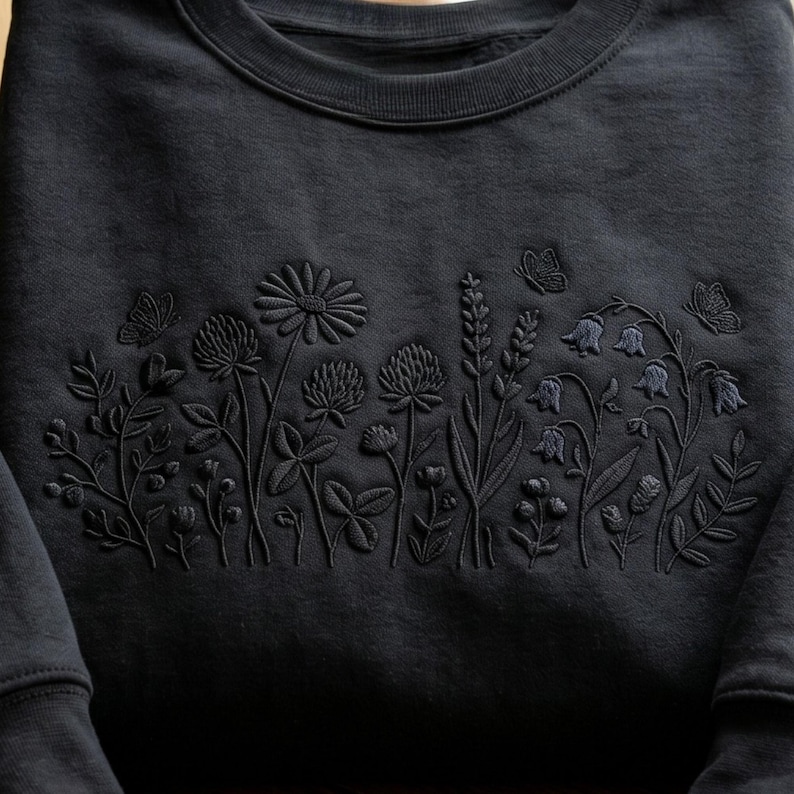 May include: Black sweatshirt with embroidered floral design. The design features various flowers, leaves, and butterflies in a tone-on-tone color scheme. The crew neck sweatshirt is made of a soft material.