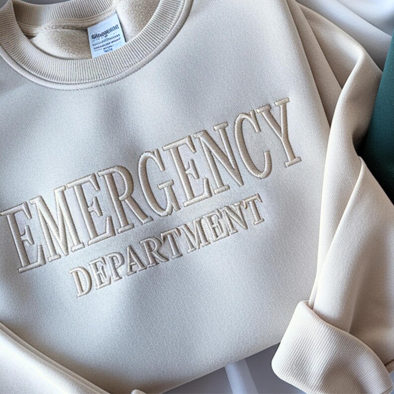 Op de afbeelding: Cr&egrave;mekleurige sweatshirt met de tekst "EMERGENCY DEPARTMENT" geborduurd. De ronde hals en manchetten zijn geribbeld. De stof is zacht en in een neutrale tint, geschikt voor casual wear.