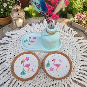 Könnte beinhalten: Ein hellblaues ovales Tablett mit einer passenden gerippten Vase, die bunte Trockenblumen enthält, sowie zwei runde Untersetzer aus Kork. Jeder Gegenstand ist mit einem rosa Flamingo-Motiv mit tropischen Blättern und Blüten verziert.