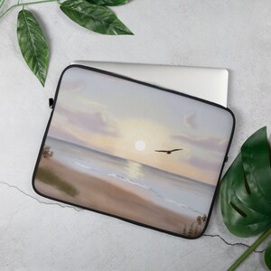 May include: A laptop sleeve with a sunset over the ocean with a bird flying in the sky. The sleeve is a light brown color with a black zipper.