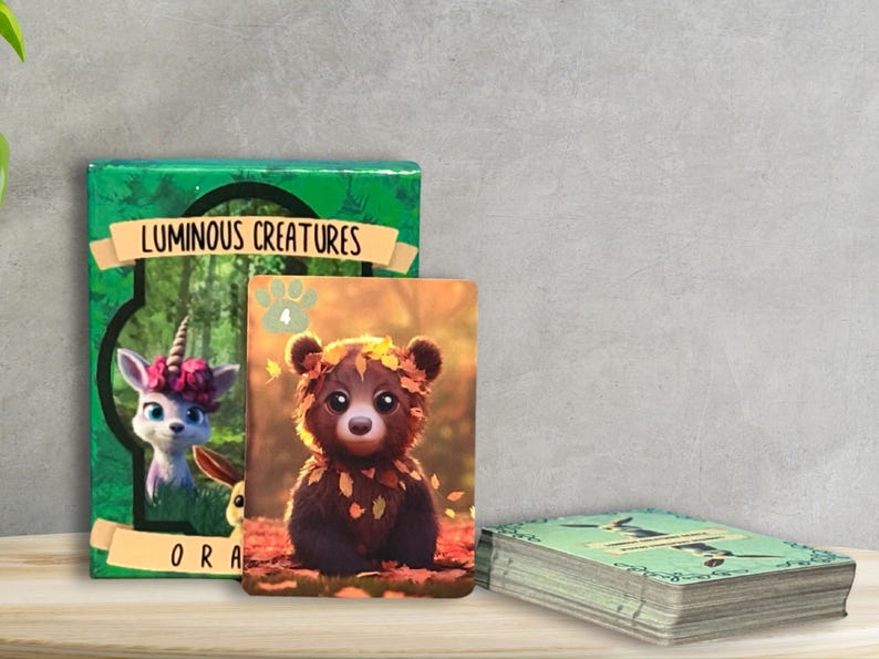 Pu&ograve; includere: Un mazzo di carte con uno sfondo verde e le parole "Luminous Creatures" sul davanti. La carta in cima presenta un orso dei cartoni animati che indossa una corona di foglie. Il retro delle carte presenta uno sfondo verde con un'impronta di zampa.