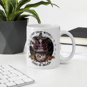 May include: White ceramic mug with a black and white illustration of a witch with a cauldron, surrounded by moons and the text "Not every witch lives in Salem".