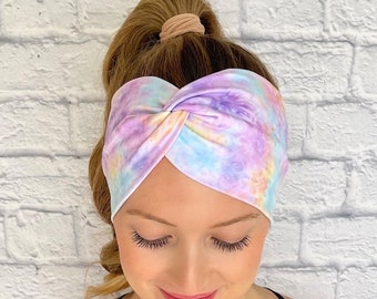 May include: A purple, pink, and blue tie-dye headband with a twisted knot design. The headband is made of a soft, stretchy fabric.