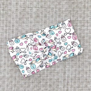 Wide, twisted headband in white with baby theme print- storks, hearts, bottles, and stethoscopes.