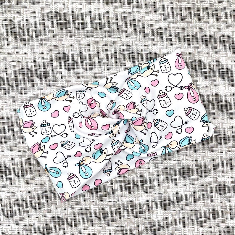 Wide, twisted headband in white with baby theme print- storks, hearts, bottles, and stethoscopes.