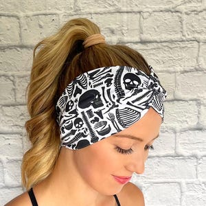 Woman with hair in curled ponytail wearing white, wide twist headband with black skeleton print.