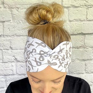 May include: White headband with a gray ribbon pattern. The headband is twisted and has a knot in the center.